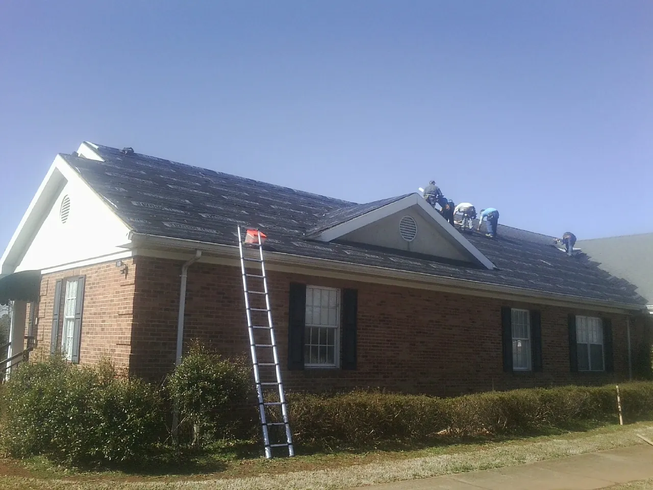 Crew tearing shingles off a brick ranch roof with a ladder set — Metal Roof Repair work by our crew in Reedsville
