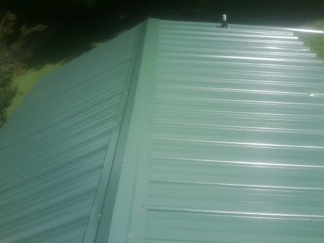 New green metal panels meeting at the ridge of a roof — Flat Roof Repair work by our crew in Reedsville
